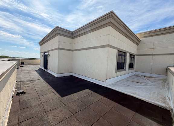 A large, empty patio area with a tiled floor and a building with a flat roof in the background.