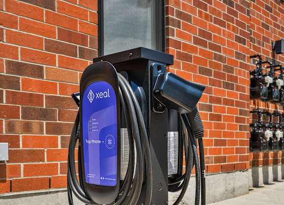 A black electric vehicle charging station with a blue screen and a long black cord.