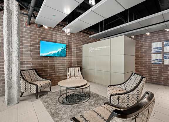 A room with a television on the wall and chairs around a table.