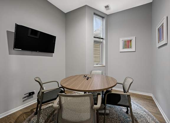 A conference room with a table, chairs, and a television mounted on the wall.