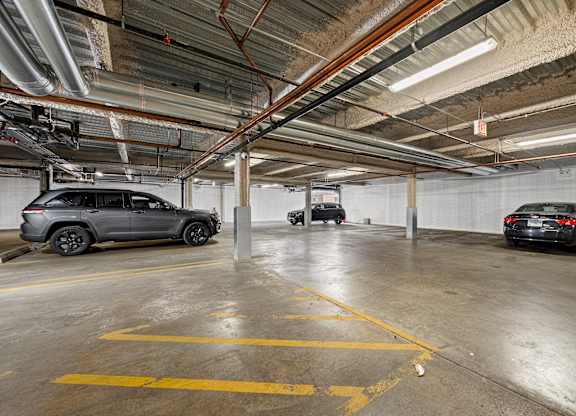 A parking garage with a grey car in the foreground and a black car in the background.