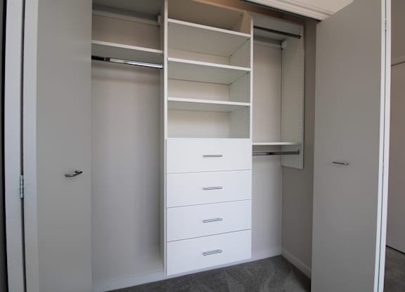 a walk in closet with white cabinets and drawers
