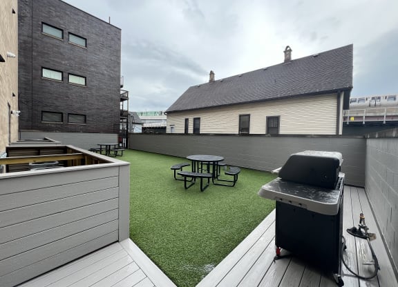 a roof deck with a grill and a picnic table on a green turf