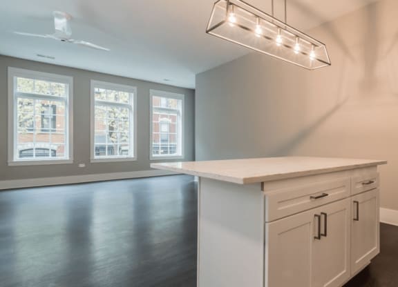 an empty kitchen with a white counter top and a light hanging above it