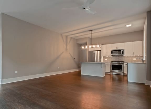 an empty living room with a kitchen in the background