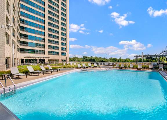 A large swimming pool with sun loungers and a tall building in the background.