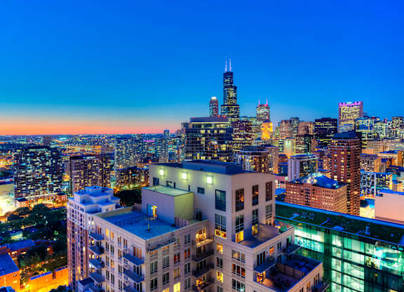 A cityscape at dusk with buildings illuminated against a darkening sky.
