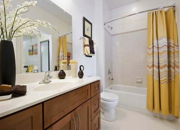 A bathroom with a white toilet, a sink with a brown towel, and a yellow shower curtain.
