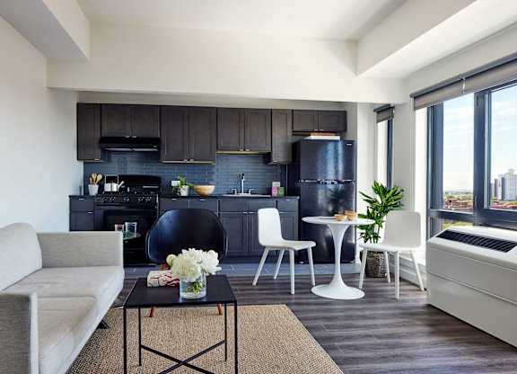 A modern living room with a grey sofa, a black coffee table, and a black kitchen area.