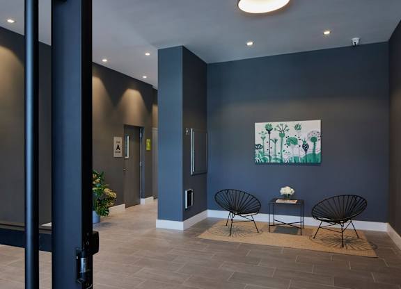 A hallway with a painting on the wall and two chairs with a table in front of them.