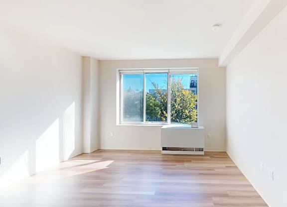A spacious room with a large window and a wooden floor.