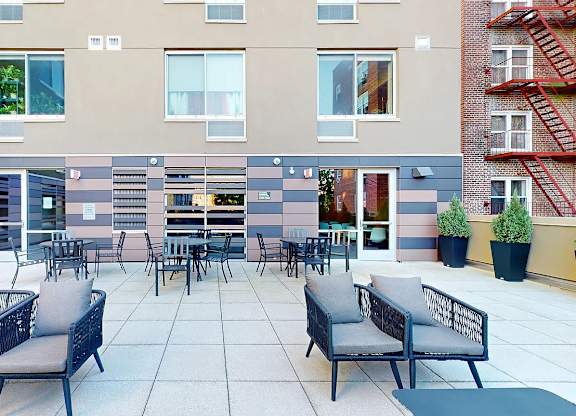 A patio with chairs and a table is surrounded by apartment buildings.