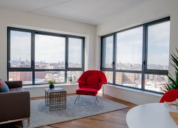 A red chair sits in a white room with a view of the city.