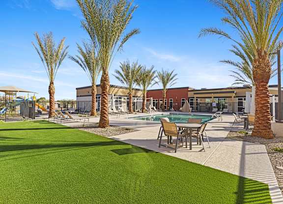 A pool surrounded by palm trees and a green lawn at Agave House Apartments, Casa Grande