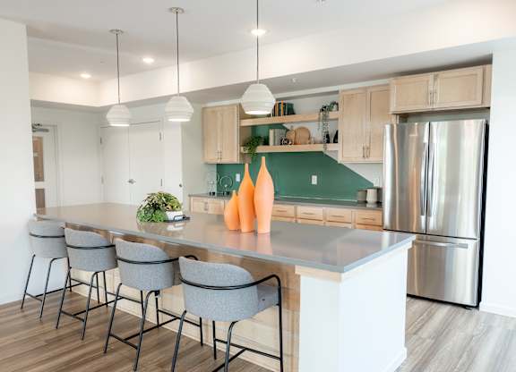 A modern kitchen with a long island and grey barstools.