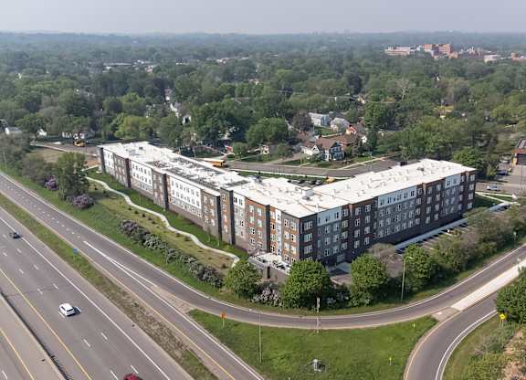 A large building with a white roof is surrounded by trees and a highway.
