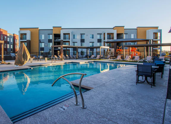 a swimming pool with chairs and umbrellas in front of an apartment building