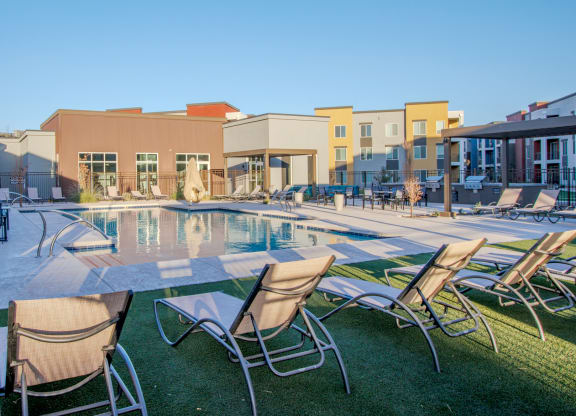 a swimming pool with chairs and a building in the background