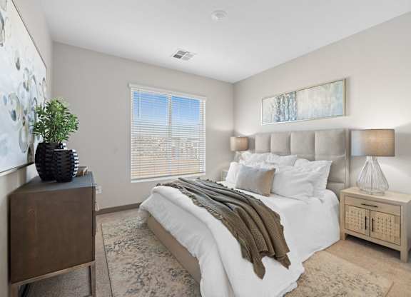 A bedroom with a large bed, a wooden nightstand, and a plant on a dresser at Copa Flats Apartments, Maricopa