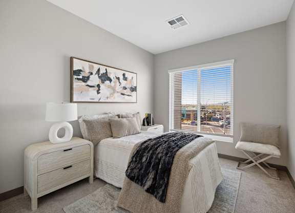 A bedroom with a large bed and a chair by the window at Copa Flats Apartments, Arizona, 85138