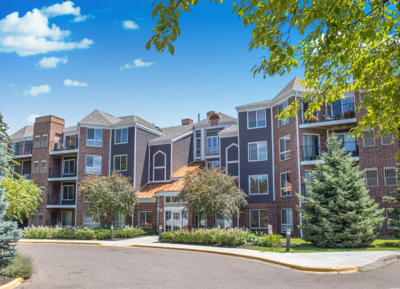 an exterior view of an apartment building with trees and a driveway