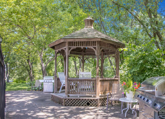 a gazebo in a backyard with trees and a grill