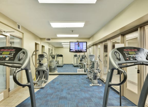 a gym with cardio machines and a tv