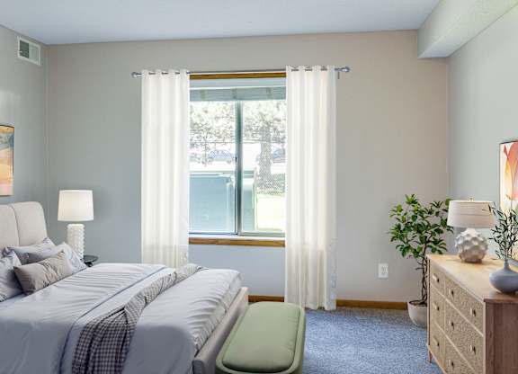 A bedroom with a bed, a chair, a nightstand, and a window with curtains. at Crosby Pointe Apartments, St. Paul , MN, 55116-3244