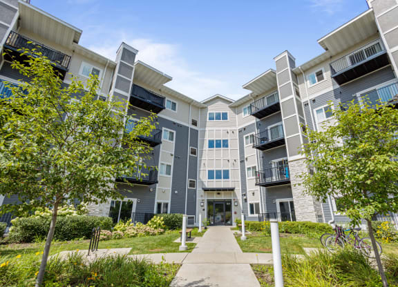 an exterior view of an apartment building with trees and a sidewalk at EastGate Apartments, Rochester, MN