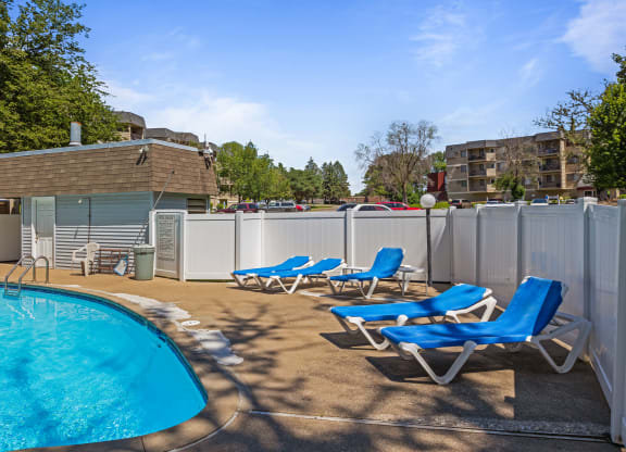 a swimming pool with blue chaise lounge chairs and a poolside building with apartments at Heritage Hills Apartments, Bloomington