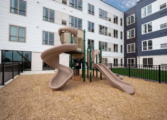 a playground with two slides and a chair in front of an apartment building at The Landing at Amber Fields Apartments, Rosemount, Minnesota
