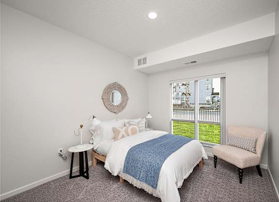 A bedroom with a large bed and a chair. at The Landing at Amber Fields Apartments, Rosemount
