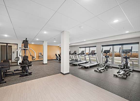 A gym with a variety of equipment including treadmills, stationary bikes, and weight machines at The Landing at Amber Fields Apartments, Rosemount, MN, 55068