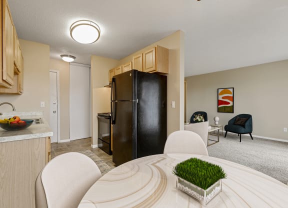 a living room with a dining room table and a kitchen with a refrigerator at Northtown Village Apartments, Spring Lake Park, 55432-2650