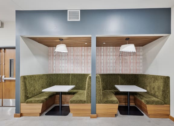 a communal seating area with two tables and green couches