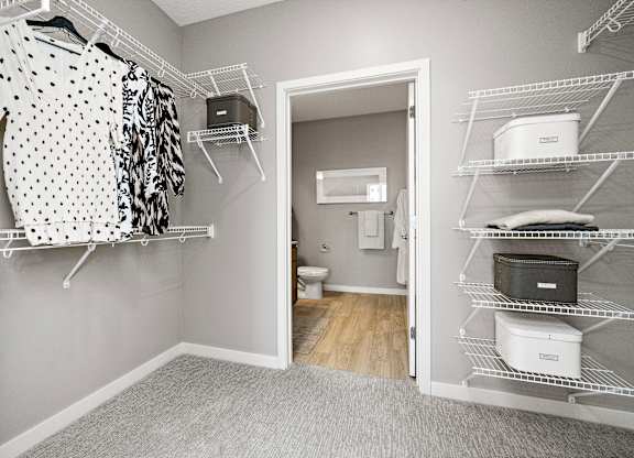 A walk in closet with clothes hanging and shelves with storage boxes.