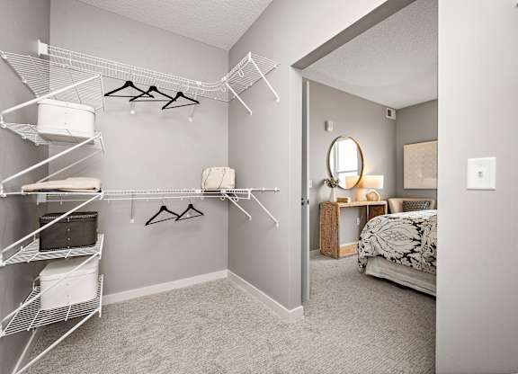 A bedroom with a bed, a mirror, and a closet with clothes hanging.