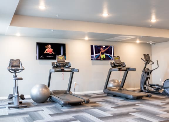 two treadmills and exercise balls in a gym with televisions at Technology Park Apartments, Minnesota