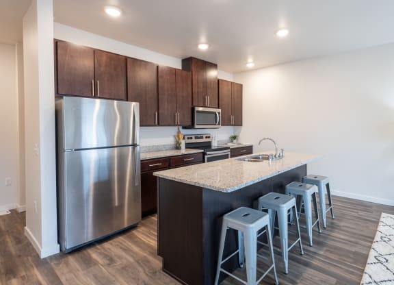 a kitchen with a large island with bar stools and stainless steel refrigerator at Technology Park Apartments, Rochester, MN