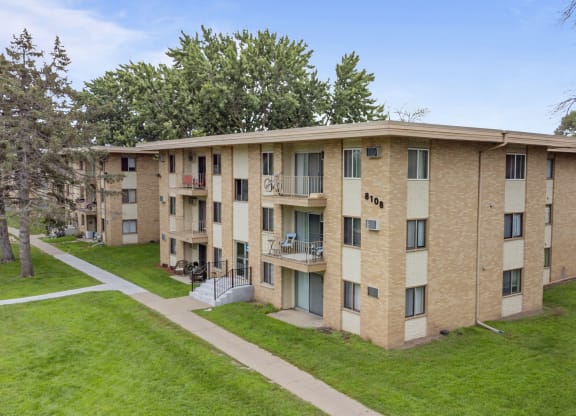 a brick apartment building with a green lawn and trees