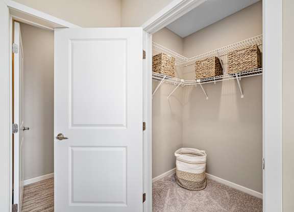 A white door is open to a bathroom with a toilet and storage baskets at The Winslow 62+ Apartments, Minnesota