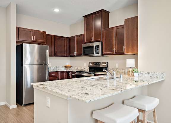 A kitchen with a granite countertop and white stools at The Winslow 62+ Apartments, West St Paul