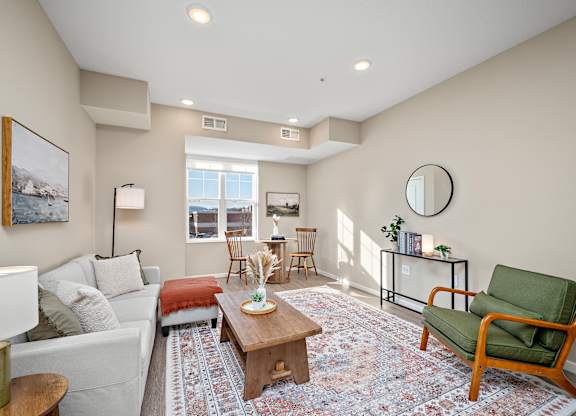 A living room with a white couch, a green chair, and a rug at The Winslow 62+ Apartments, West St Paul
