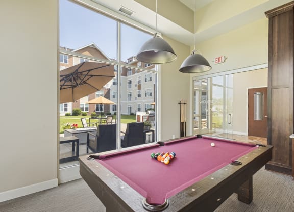 a pool table in a clubhouse with two lights hanging over it at The Winslow 62+ Apartments, West St Paul, Minnesota