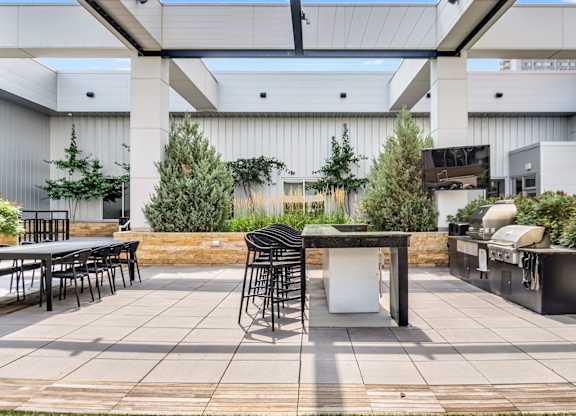A patio with a table and chairs is surrounded by green plants.