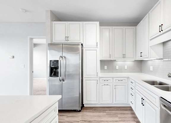 A white kitchen with a refrigerator, cabinets, and a sink.