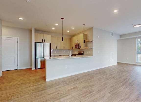 an empty living room with a kitchen and a large window