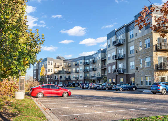 A red car is parked in a parking lot in front of apartment buildings.