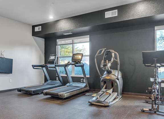 A gym room with treadmills, exercise bikes, and a television.