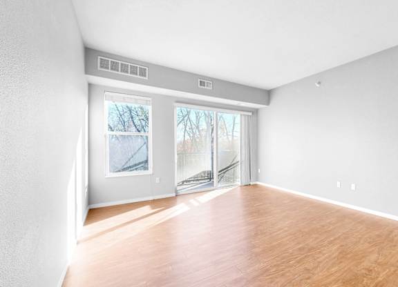A room with wooden floors and white walls, with a sliding glass door leading outside.